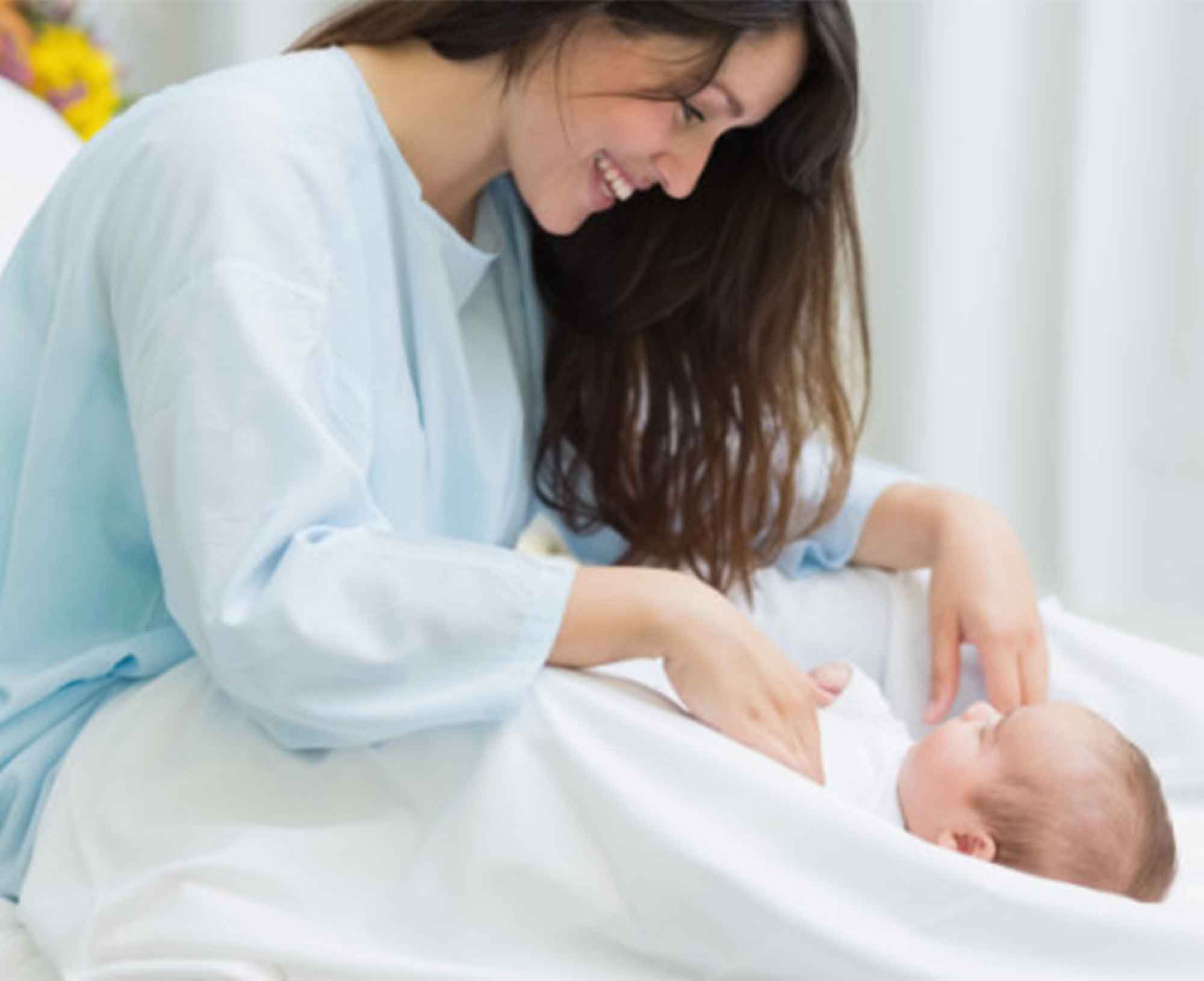Mother in a hospital gown looking at her newborn baby