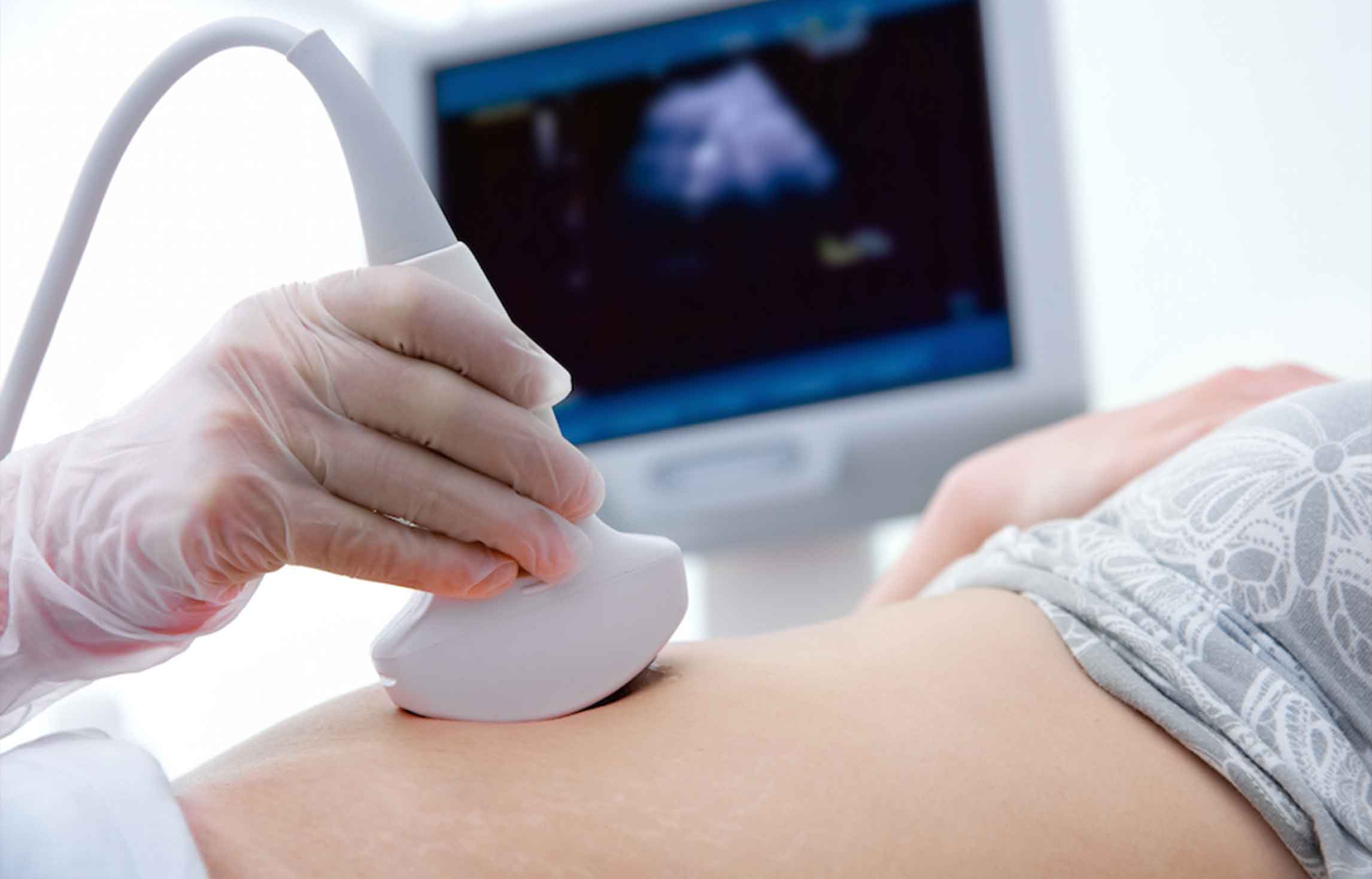 Gloved hand moving an ultrasound probe across a patient's abdomen