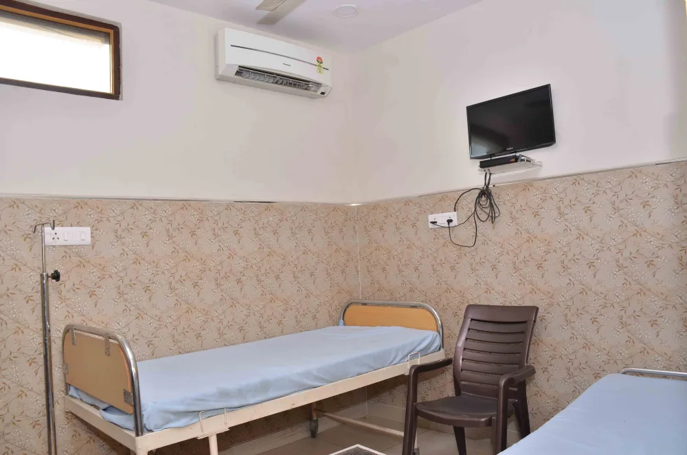 Hospital bed beside a chair with a wall-mounted television and air conditioner