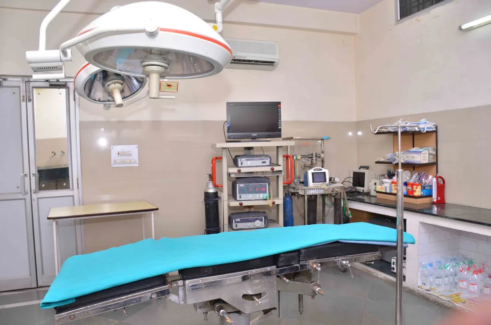 Large surgical light above a blue operating table with monitors behind it